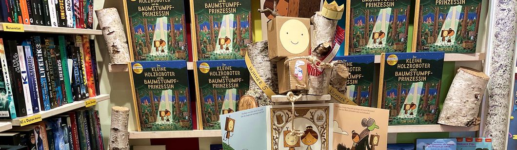 Im Buchpalast: Der kleine Holzroboter aus Pappkarton hält seine Baumstumpfprinzessin aus Birkenholz im Arm
